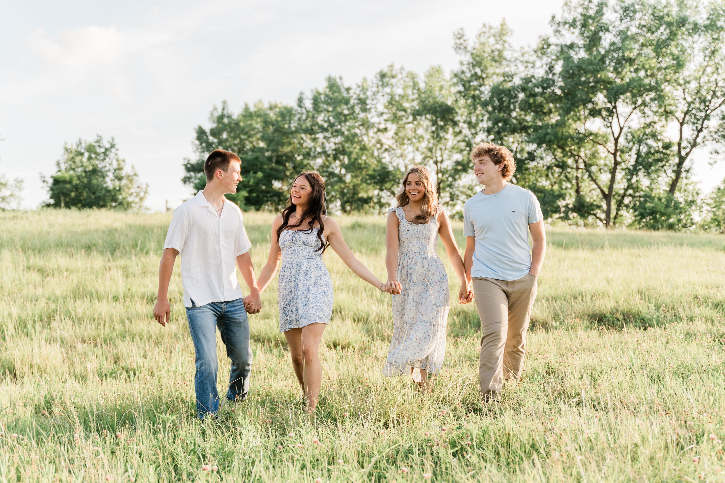 A group walks through a sunlit meadow holding hands on a warm summer day.