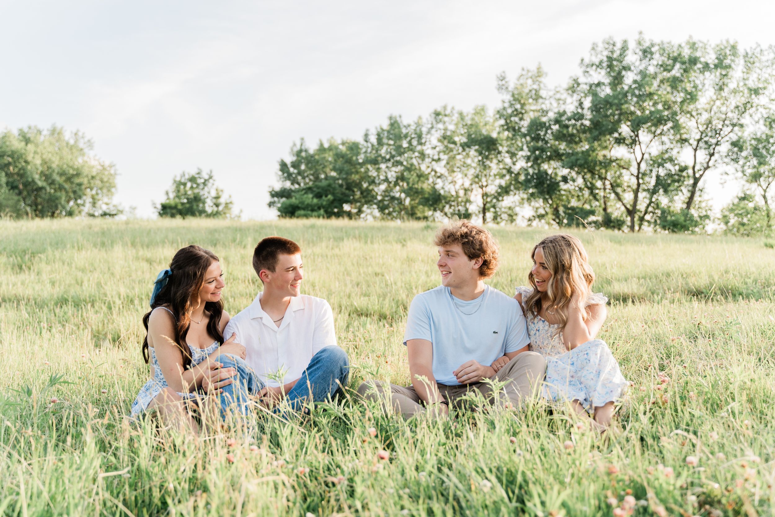 A group of people sit together laughing and enjoying a sunny summer day in a grassy field.