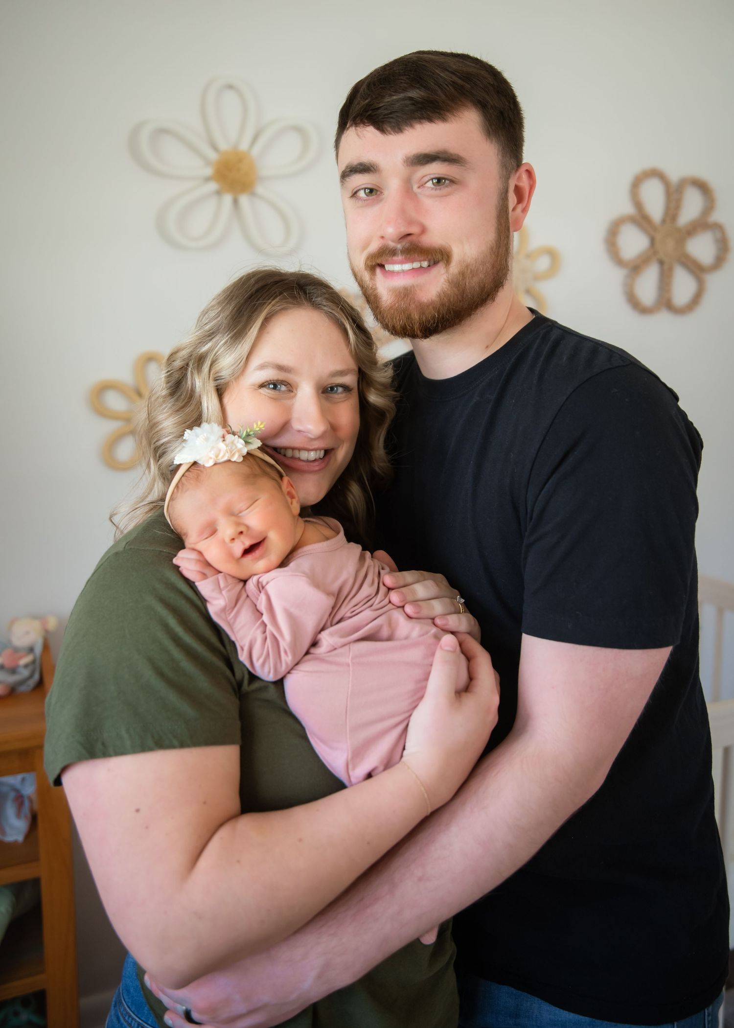 A happy family shares tender hugs and loving moments while wearing casual attire against a light colored wall with floral decor.