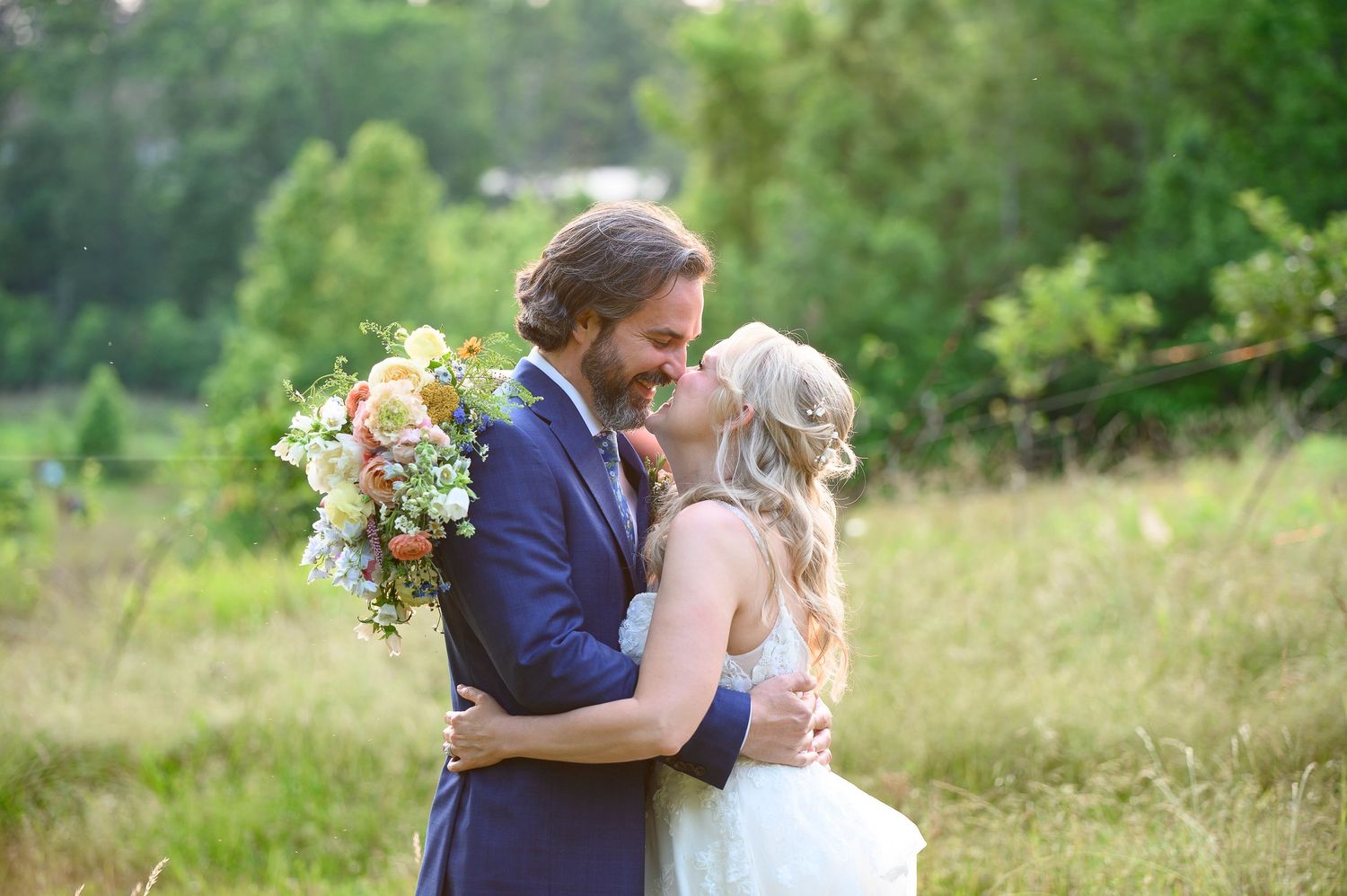 A couple embraces in a sunlit meadow during a summer wedding, with a colorful bouquet of flowers. waleska ga wedding photographer
