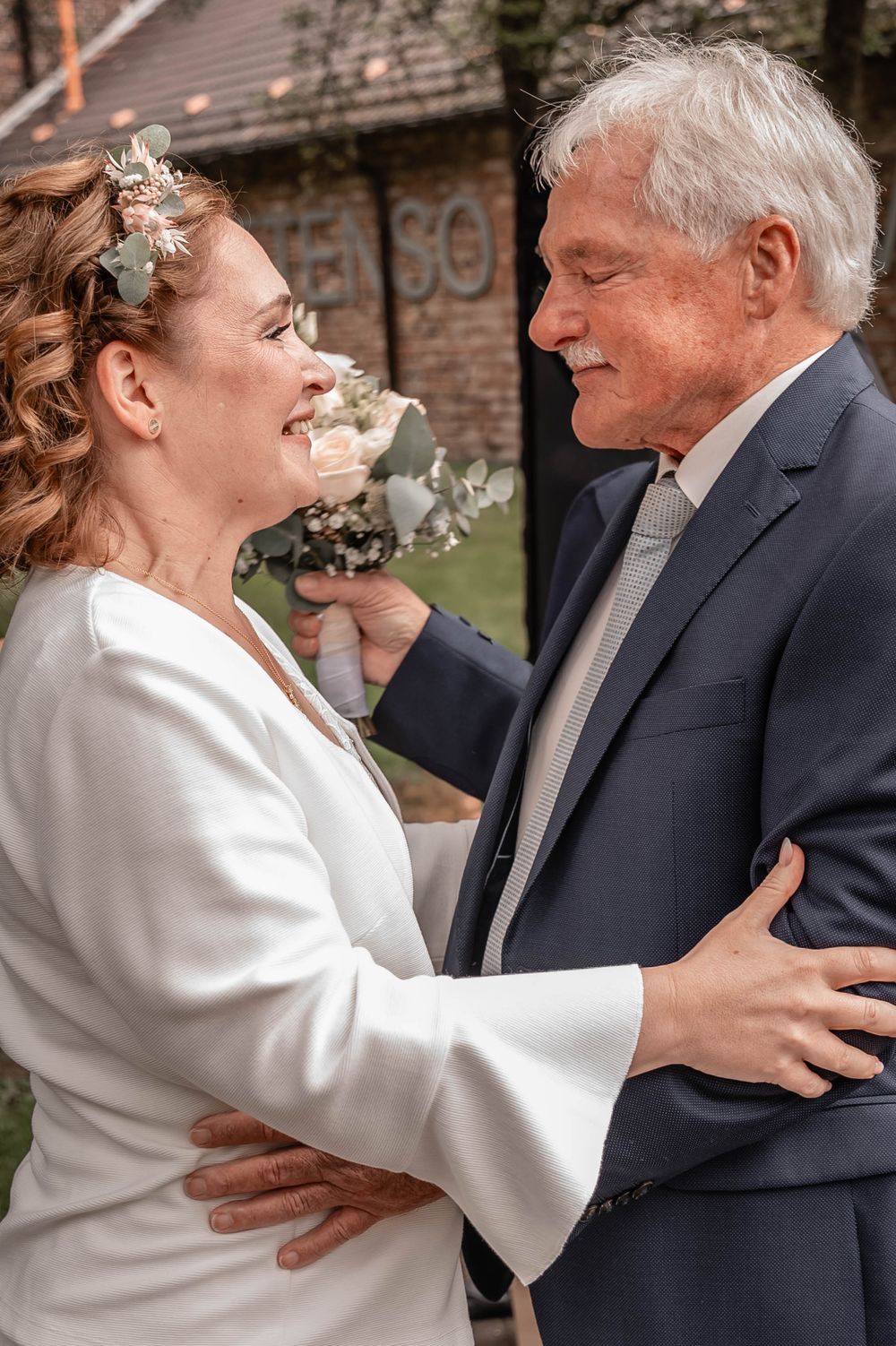 A heartwarming moment between a couple in wedding attire, sharing laughter and embraces outdoors.