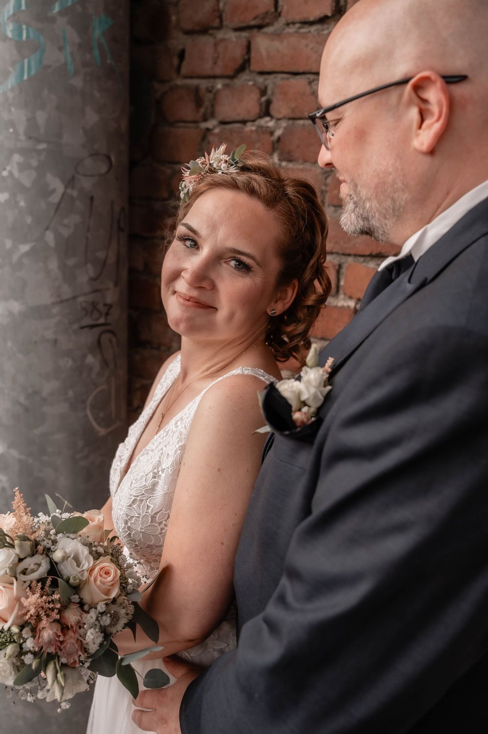 A bride and groom share intimate moments against a rustic brick wall backdrop during their wedding photoshoot.
