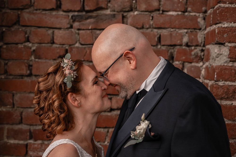 Bride and groom share romantic moment in front of rustic brick wall during wedding photoshoot.