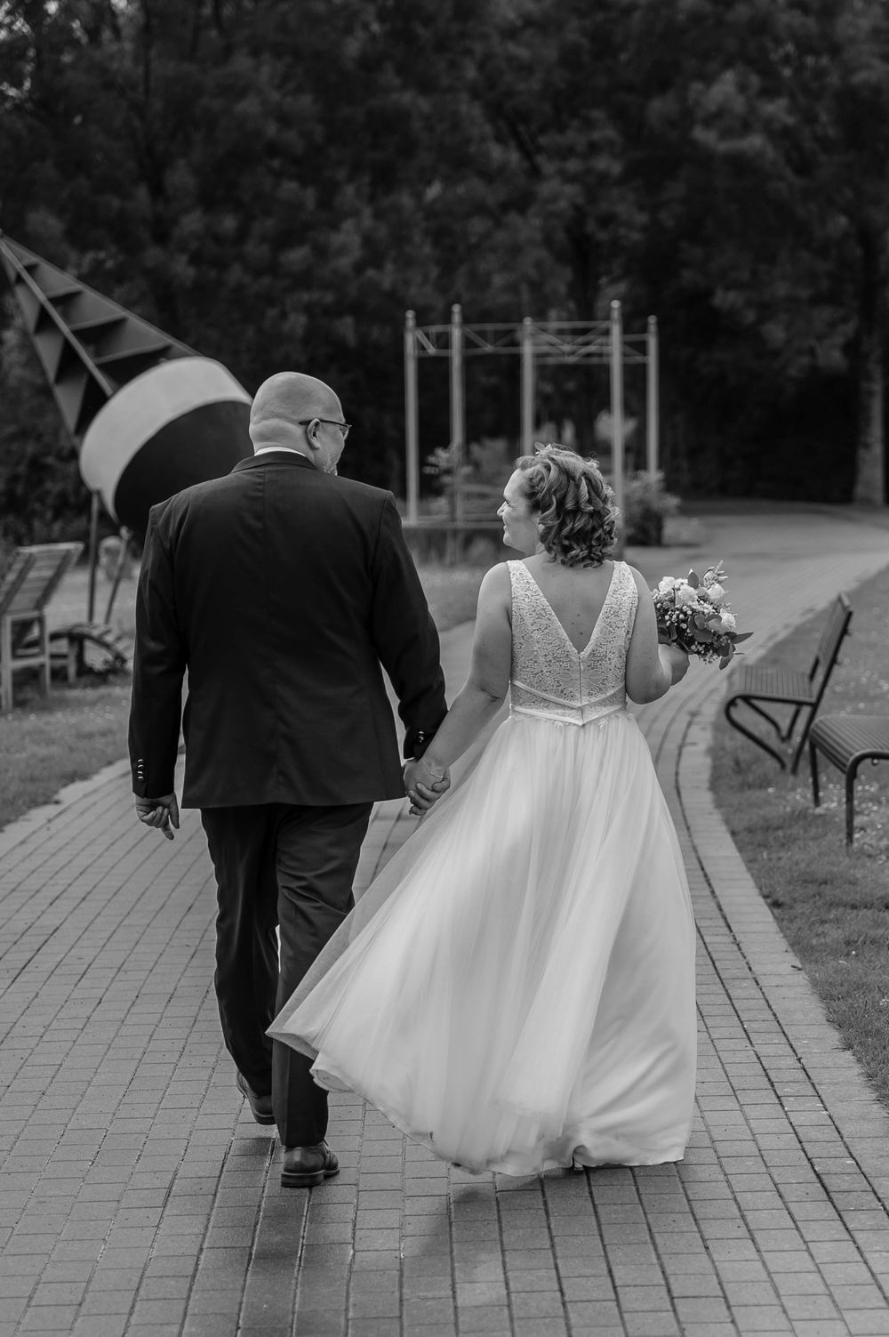 A couple in wedding attire walking down a brick path, captured in black and white photography.