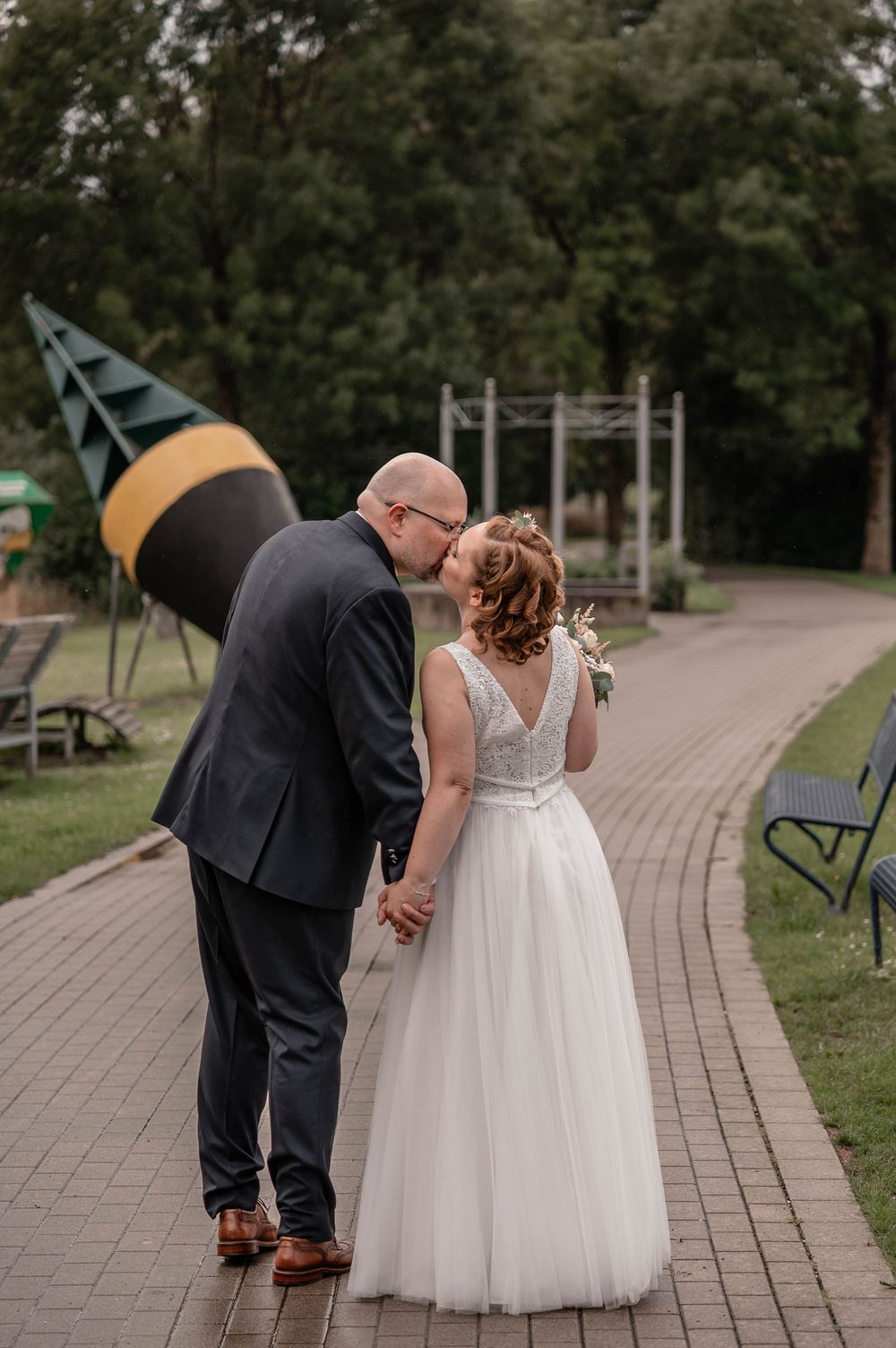 Romantic wedding couple sharing sweet kisses while walking along a curved brick pathway in a garden setting.