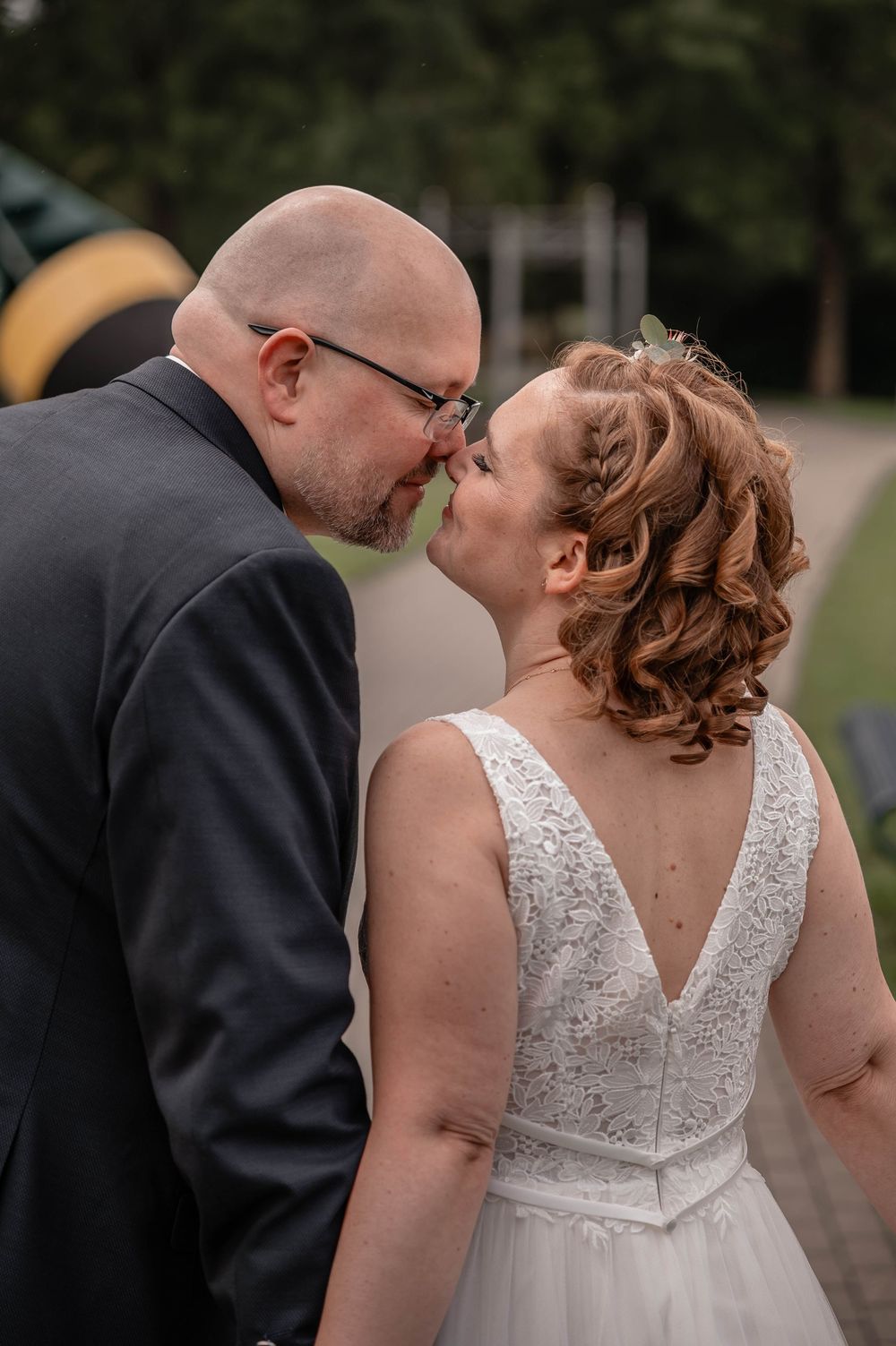A tender moment between newlyweds as they share a kiss outdoors, with the bride wearing a white lace dress.
