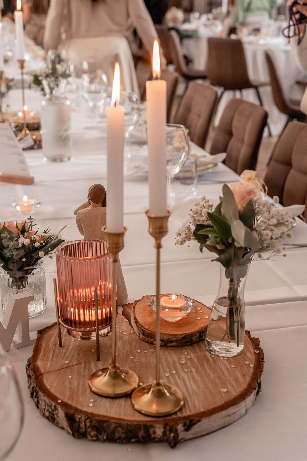 Rustic wedding centerpiece with white candles and pink glass votives on a wood slice base with delicate floral accents.