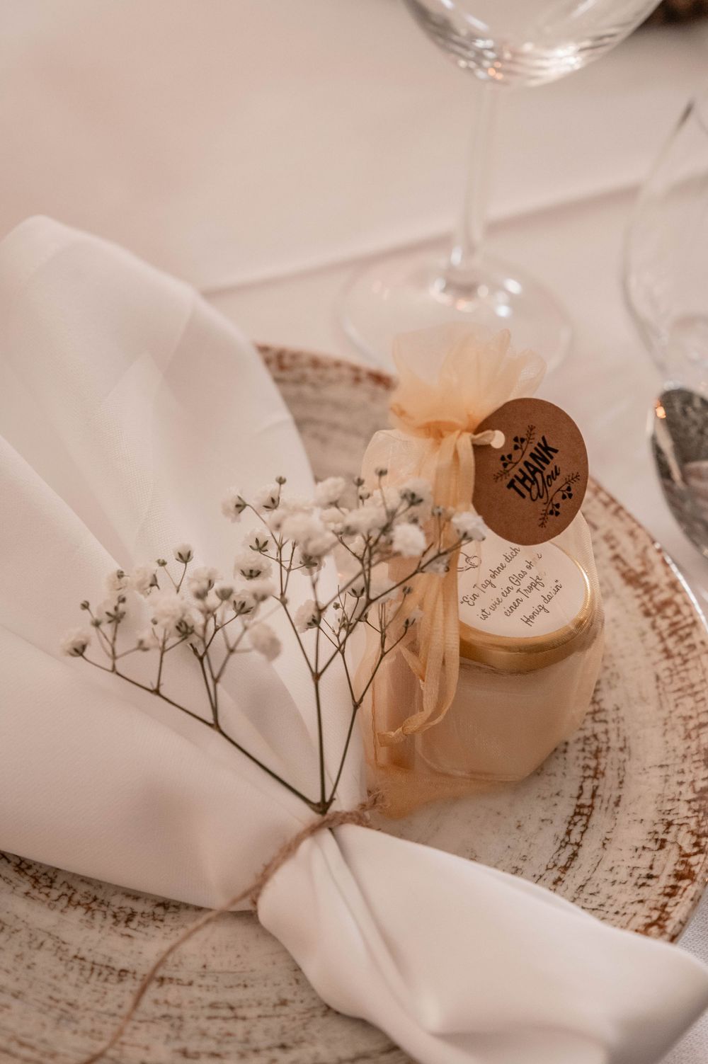 Elegant table setting with white linen napkin decorated with baby's breath flowers and small glass jar favors on rustic plate.