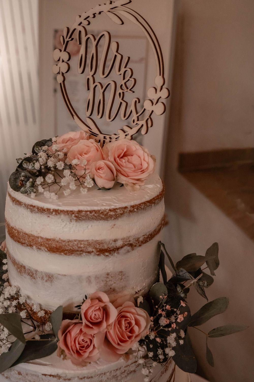 Close-up collage of white wedding cake with pink roses and delicate greenery decoration displayed from different angles.