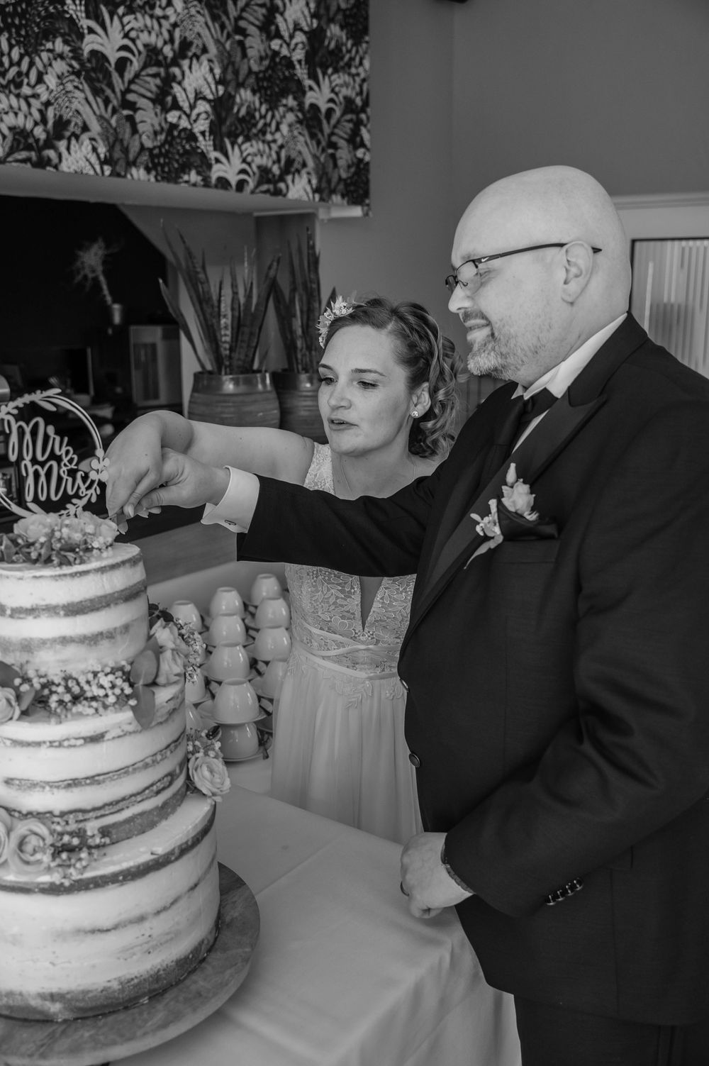 A black and white wedding photo of a couple cutting their elegant three-tiered semi-naked cake at their reception.