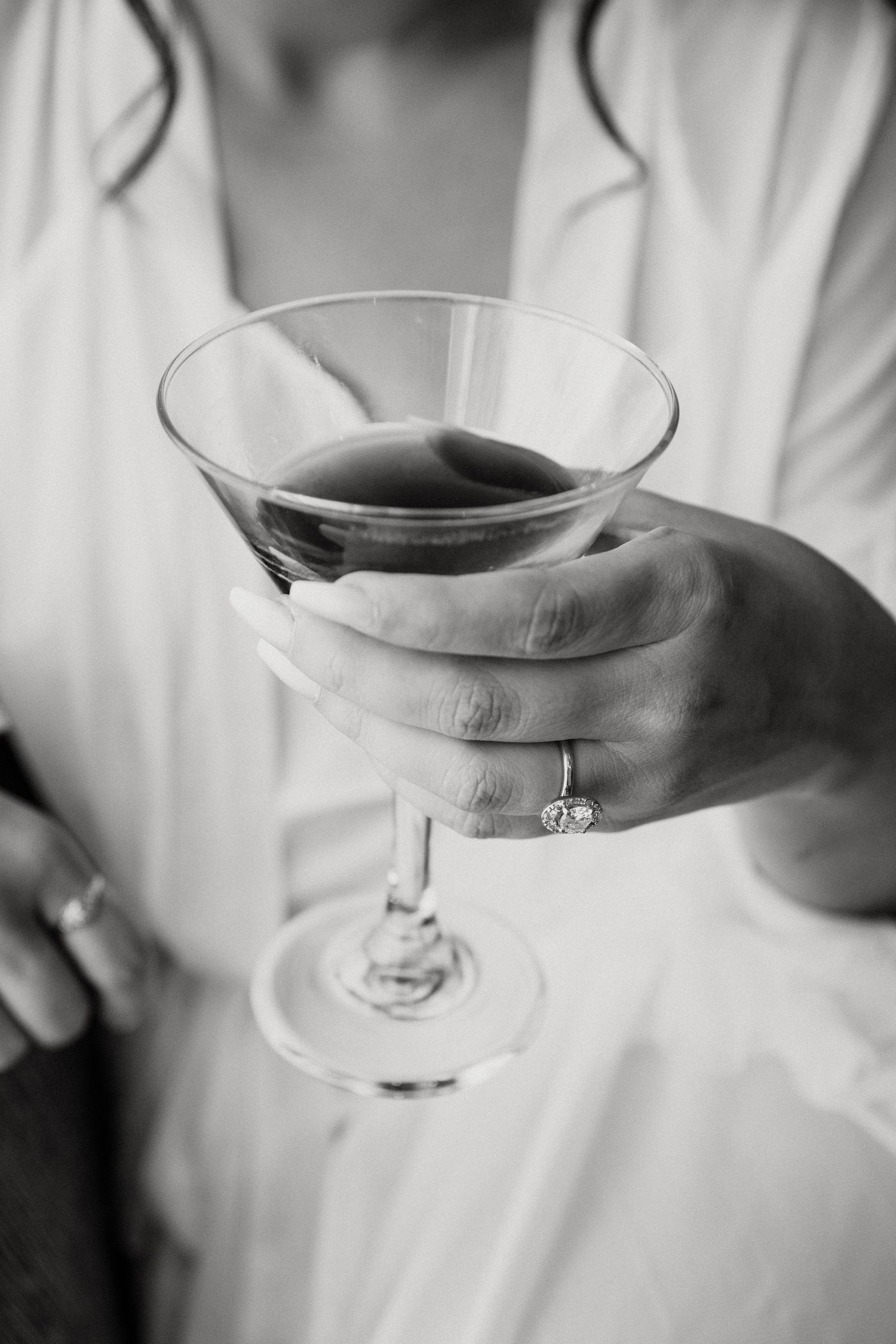 Black and white detail shot of hand holding martini glass during wedding celebration.