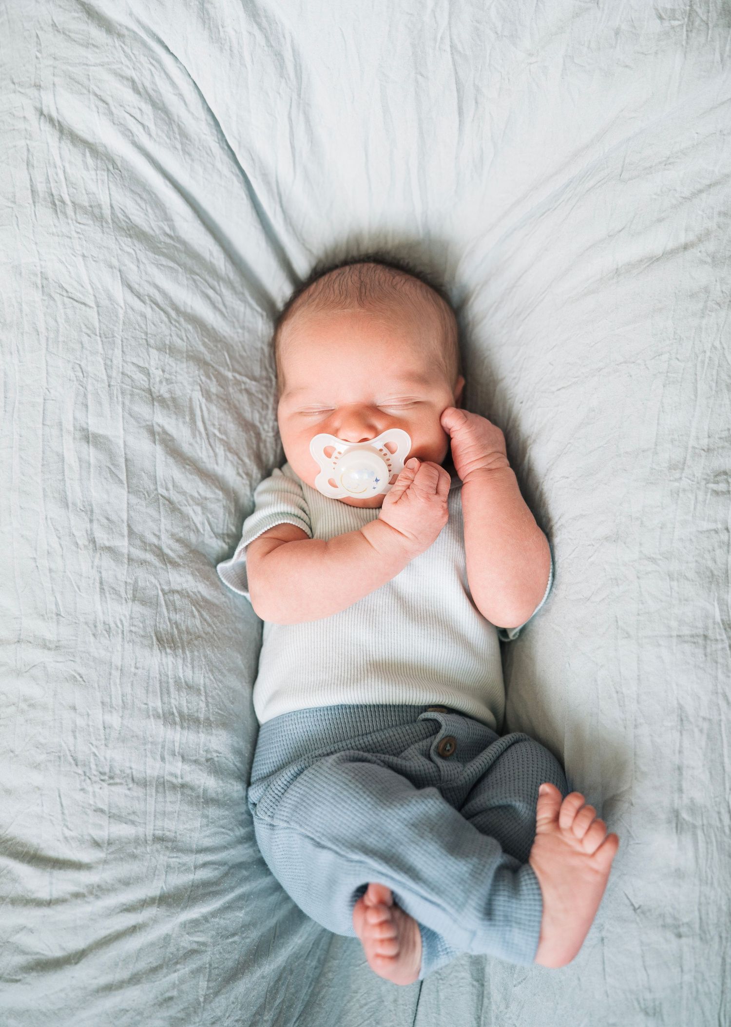 A newborn baby with a pacifier lays on a dock a tot sleeping while a solano county photographer photographs him