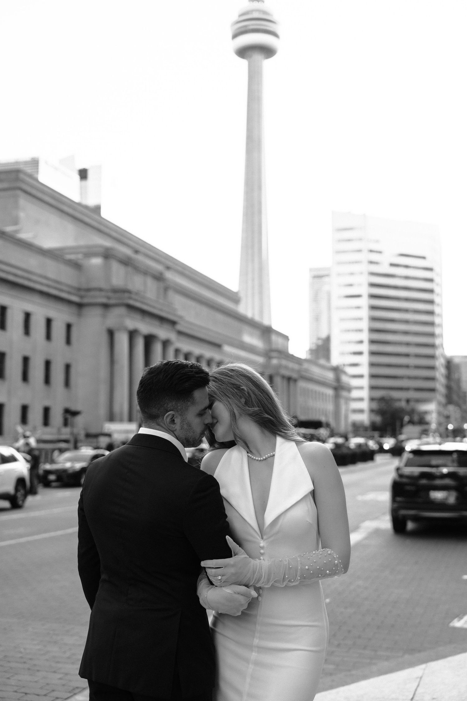 A romantic black and white series of photos showing a couple in formal attire kissing near urban architecture.