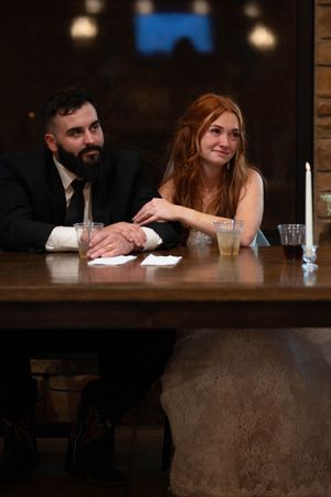 Wedding party members sit at rustic bar with brick wall and dim lighting in background.
