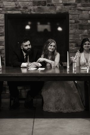 Black and white photo of wedding party members gathered at rustic bar with stone walls.
