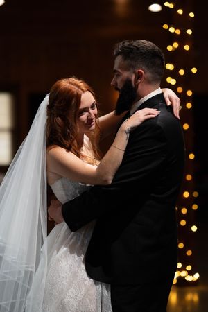 Romantic first dance moment captured with twinkling lights in background at wedding reception.