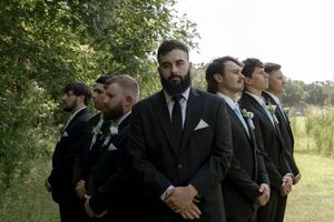 Groomsmen in black suits pose together outdoors.