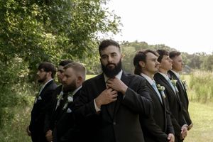 Groomsmen in black suits share candid moments outdoors during a wedding photo session.