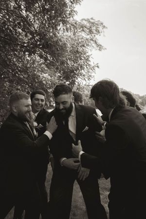 Wedding party members in formal black attire interact in a dramatic black and white photo.