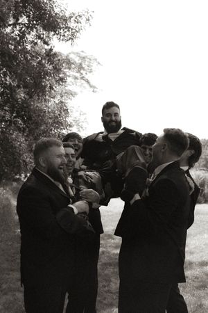 Black and white photo of groomsmen in suits playfully posing outdoors.