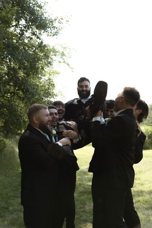 Wedding party members in dark suits having fun with casual group photos outside.