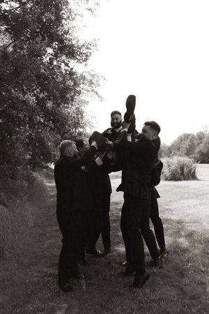 Groomsmen in black suits playfully pose together outdoors in a candid moment.