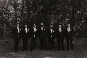 Wedding party lined up in formal black attire against a natural outdoor backdrop.