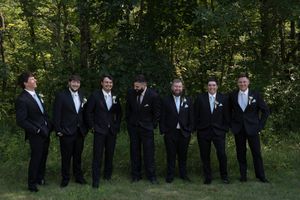 Groomsmen in matching black suits and white boutonnieres stand in formation for a formal photo.