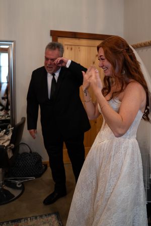 A bride in a white lace gown shares an intimate moment during wedding preparations.