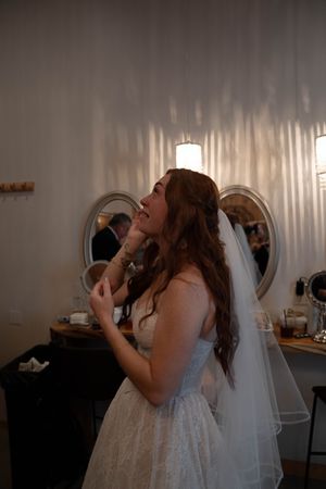 A bride in a white dress takes a drink during wedding preparations.