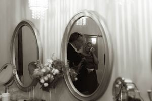 A bride in a white dress and veil takes a drink while getting ready.