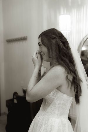 A bride in a lace wedding dress wipes her face during an emotional moment.