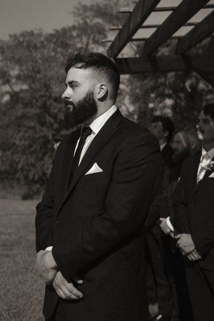 Wedding party members in formal black suits stand together during outdoor photography session.