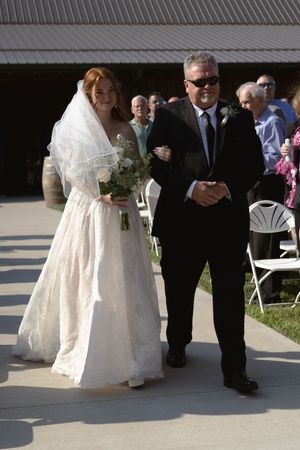 A bride in a white gown walks down an outdoor aisle with her escort.