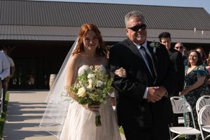Wedding guests gather outside on a sunny day near a building with white chairs set up.