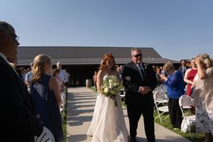Wedding attendees gather on a concrete path during an outdoor ceremony.