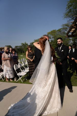 An outdoor wedding ceremony setup with white chairs and a wooden pergola against a blue sky.