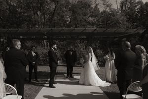 Outdoor wedding ceremony setup with guests seated beneath trees.
