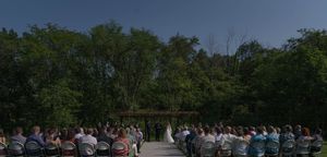 Wide view of an outdoor wedding ceremony with guests seated in white chairs.