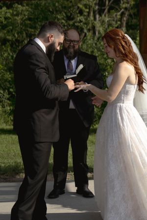 A wedding ceremony moment captured under a wooden pergola with guests watching.