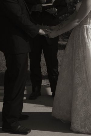 Close-up black and white shot of wedding ceremony feet showing bride's white dress and groom's formal shoes.