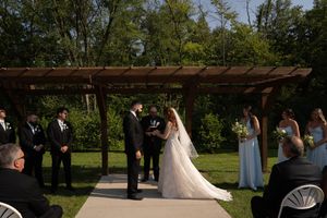 Wedding ceremony in progress with bridal party and guests gathered under a wooden pergola.