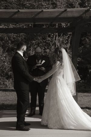 Wedding ceremony proceedings under covered outdoor venue with officiant and couple.