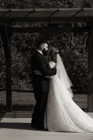 Black and white photo of newlyweds embracing under a covered outdoor ceremony space.