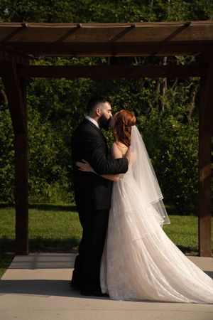 Couple shares their first kiss as newlyweds under a rustic wooden pergola.