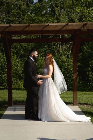 Outdoor wedding ceremony under wooden pergola with natural greenery in background.