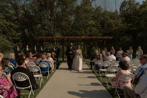 Wedding guests seated in white chairs for an outdoor ceremony with trees in the background.