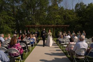 Wedding ceremony recessional with guests seated in white chairs along an outdoor aisle.