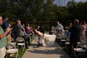 Wedding guests mingle during an outdoor reception with white chairs and natural scenery.