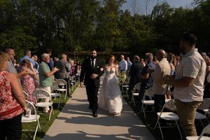 Outdoor wedding reception with guests gathering on a paved pathway surrounded by greenery.